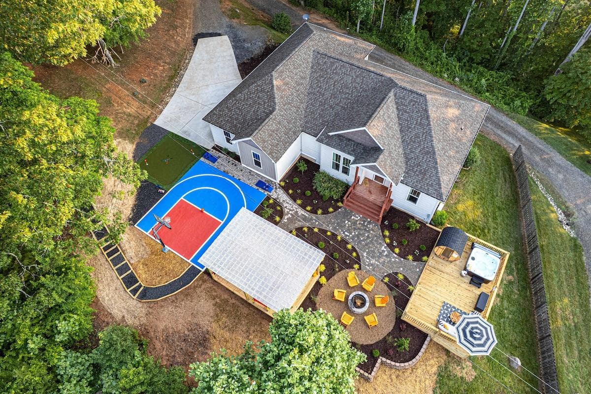An aerial view shows off the retreat’s epic layout: basketball court, mini golf, sauna, hot tub, firepit, and winding paths—all centered around a luxury home nestled at the edge of peaceful woods. Space, style, and play—it's all here.